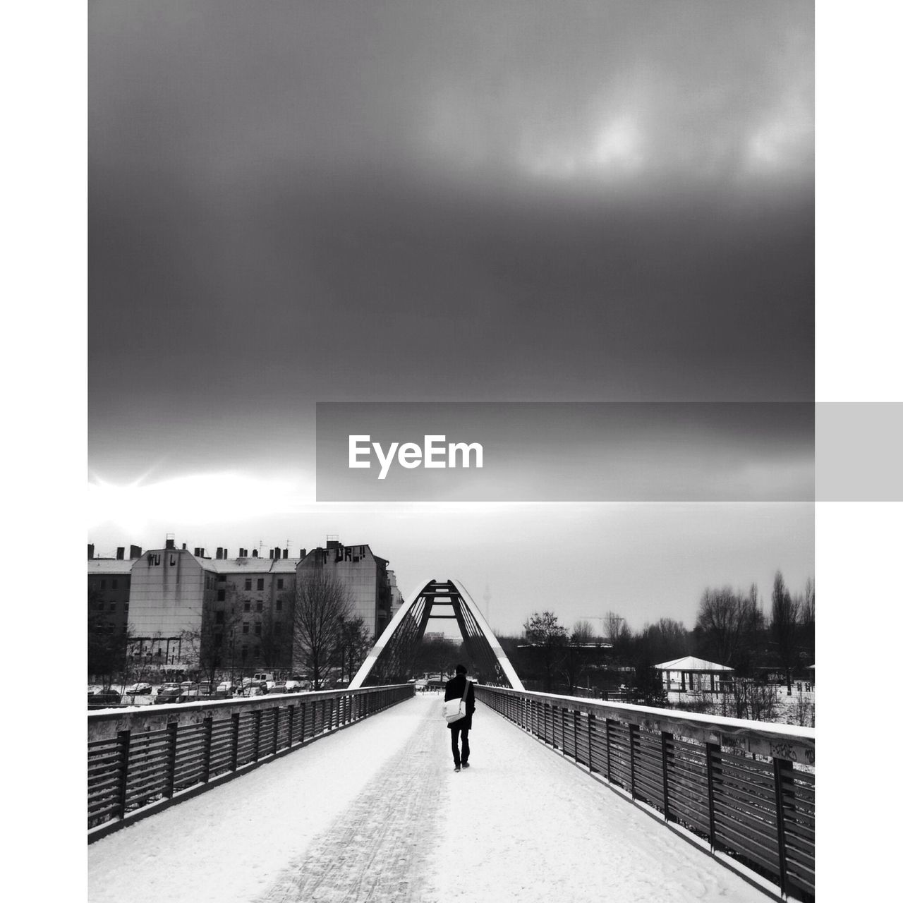 Rear view of person walking on snow covered bridge against cloudy sky