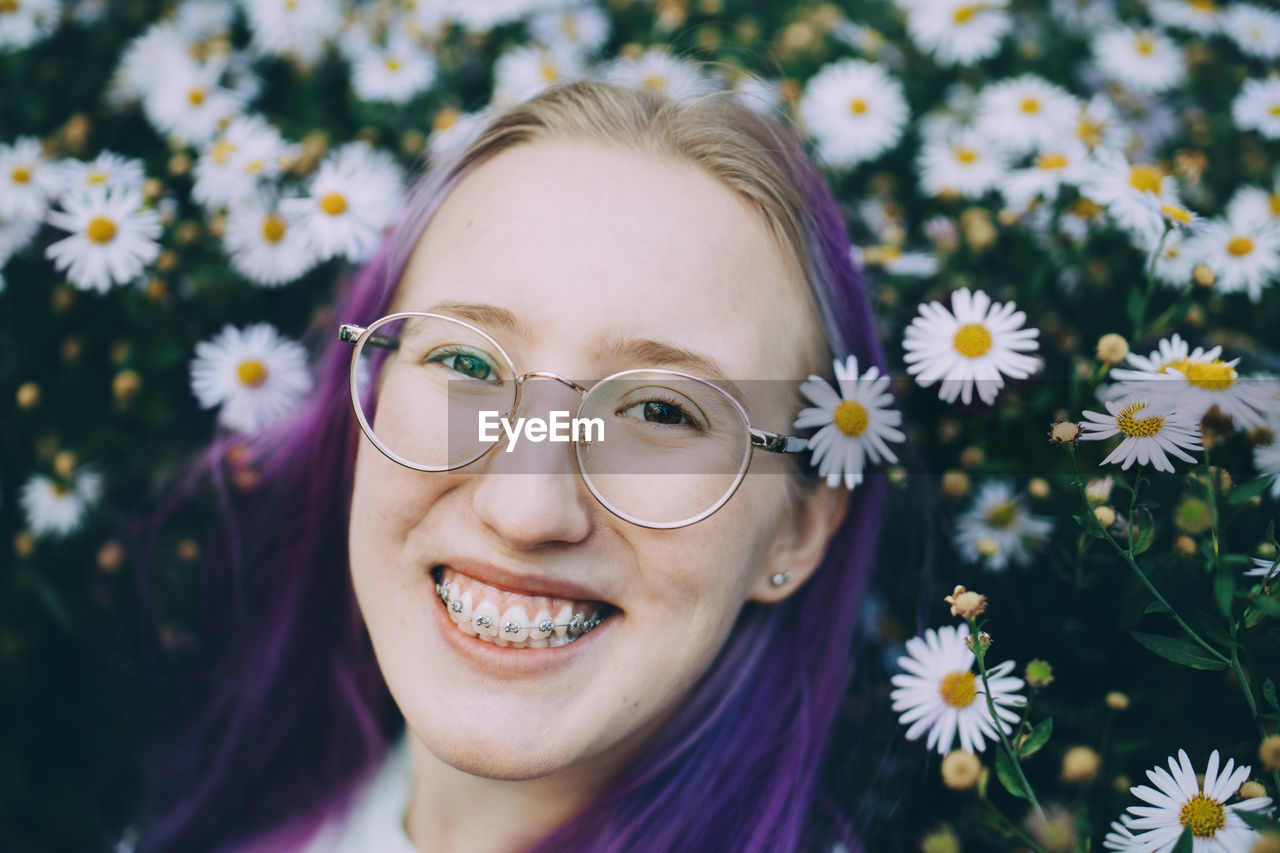 Portrait of smiling teenage girl with braces amidst daisy flowering plants