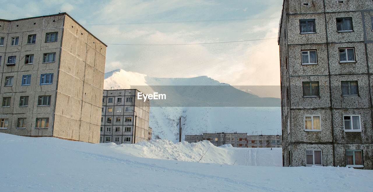 Snow covered buildings by mountain against sky