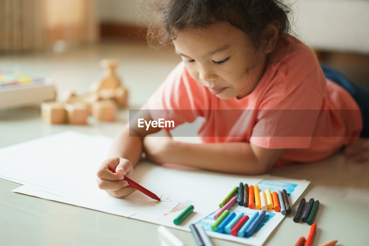 Girl coloring on paper while lying at home