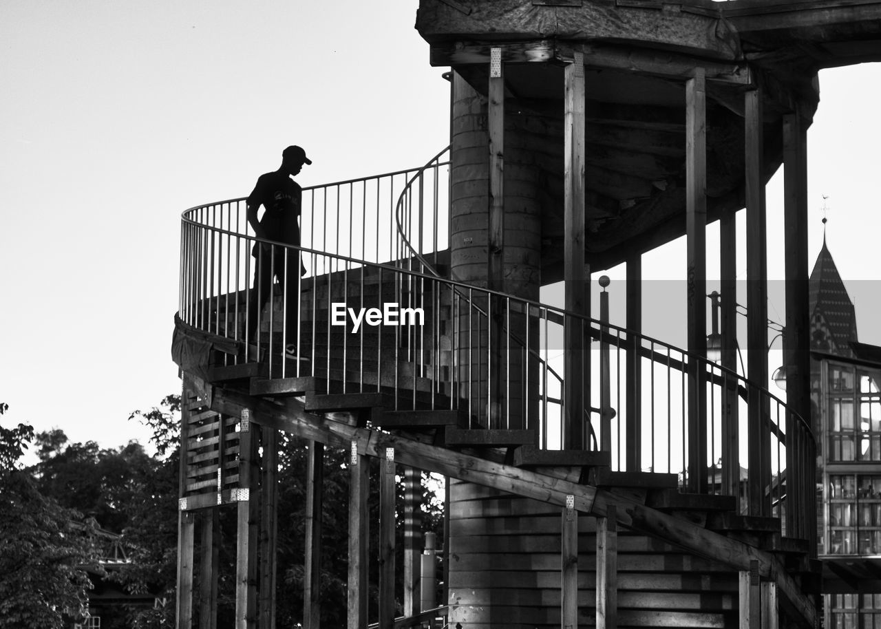 LOW ANGLE VIEW OF MAN STANDING BY STAIRCASE AGAINST BUILDING