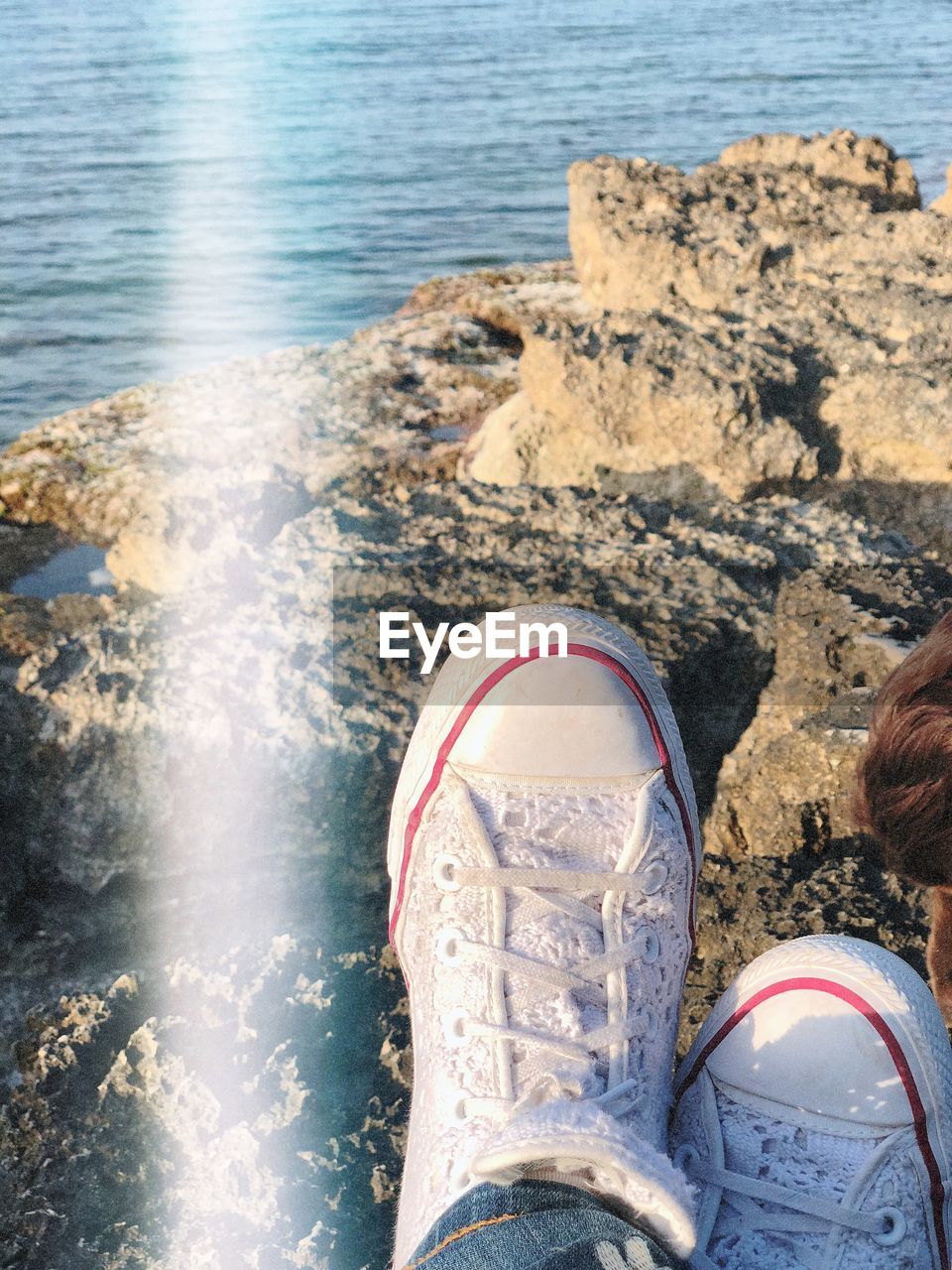 LOW SECTION OF PERSON STANDING ON ROCK IN SEA