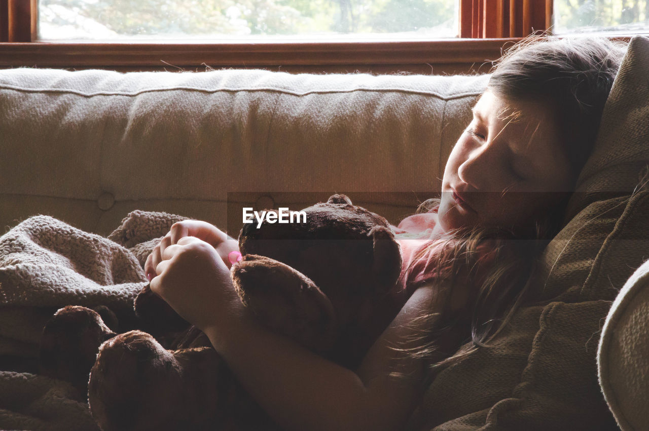 Girl sleeping with teddy bear on sofa at home