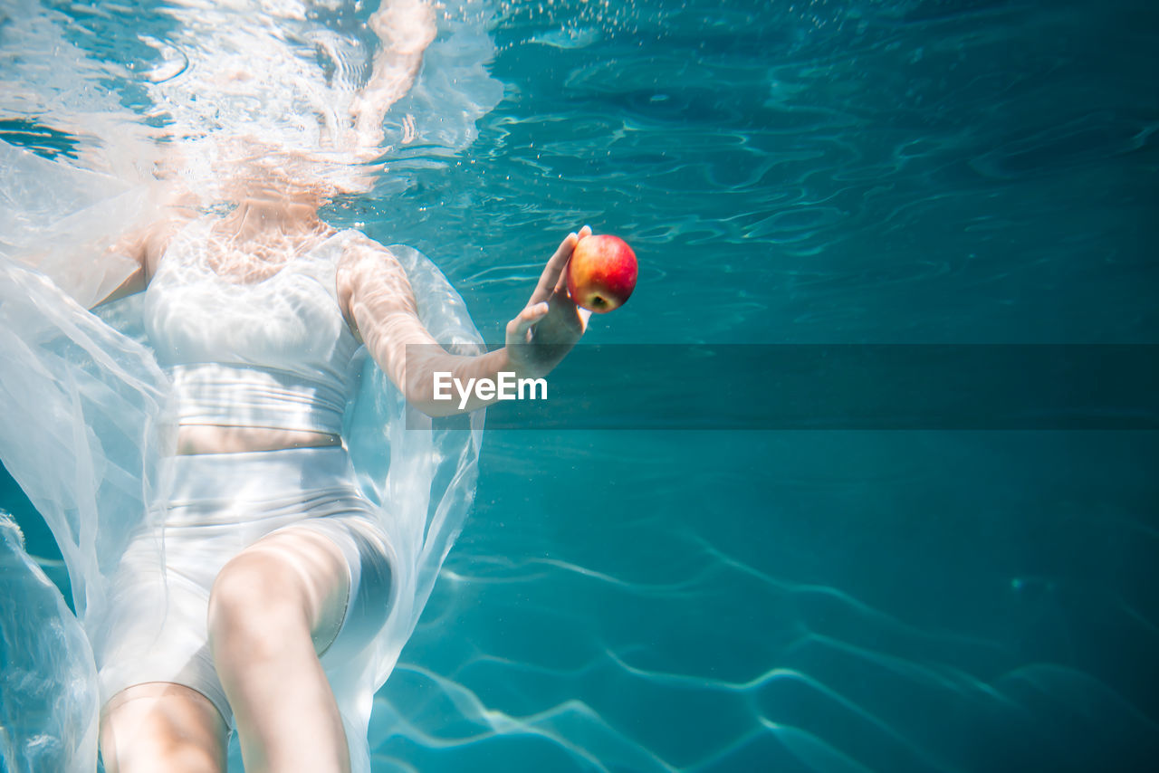 Midsection of woman holding apple underwater in swimming pool