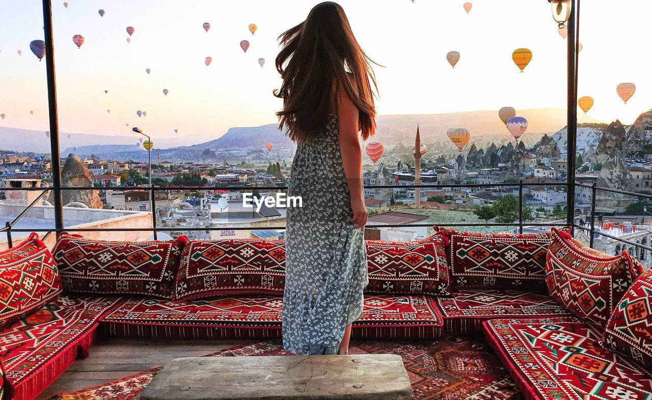 REAR VIEW OF WOMAN STANDING AGAINST SKY IN CITY