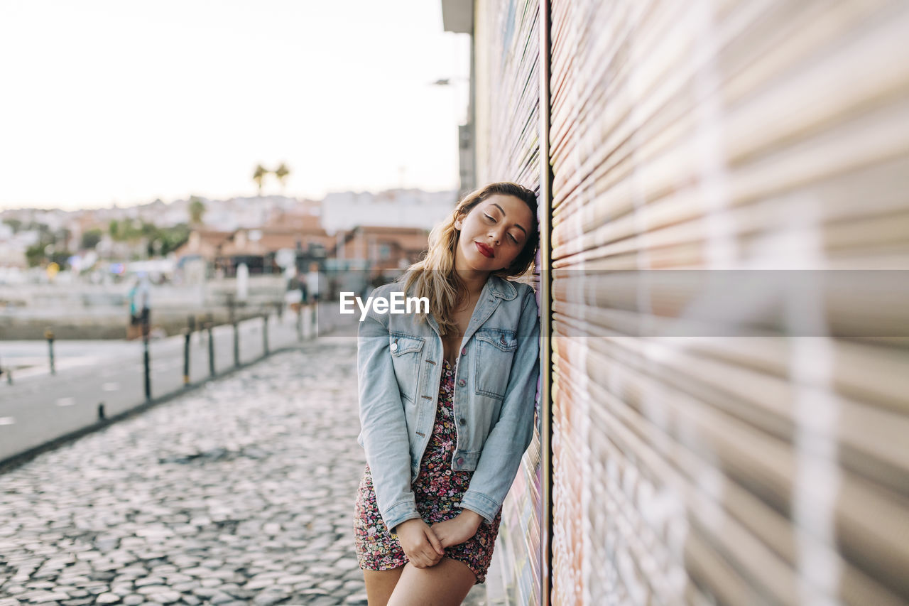 Young woman leaning on wall on footpath