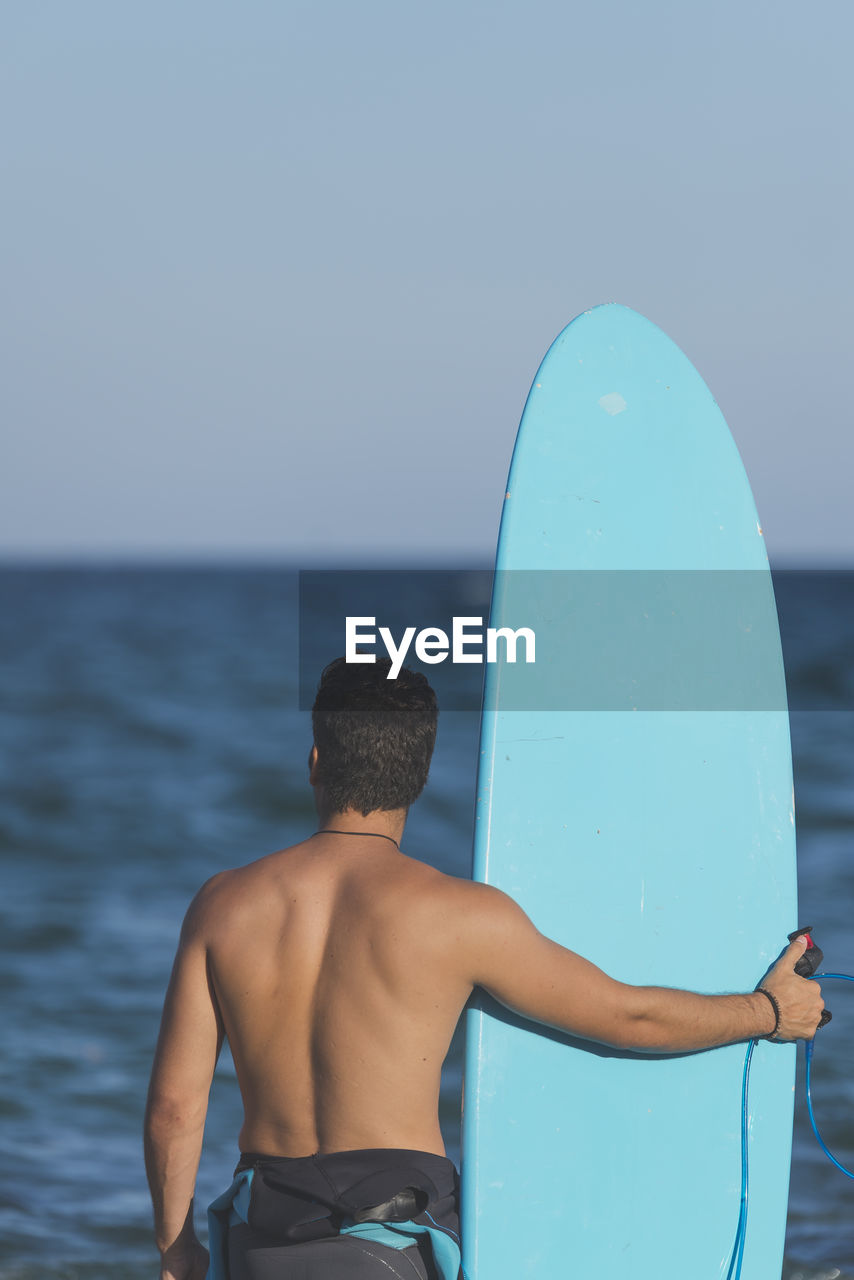 Shirtless man with surfboard at beach