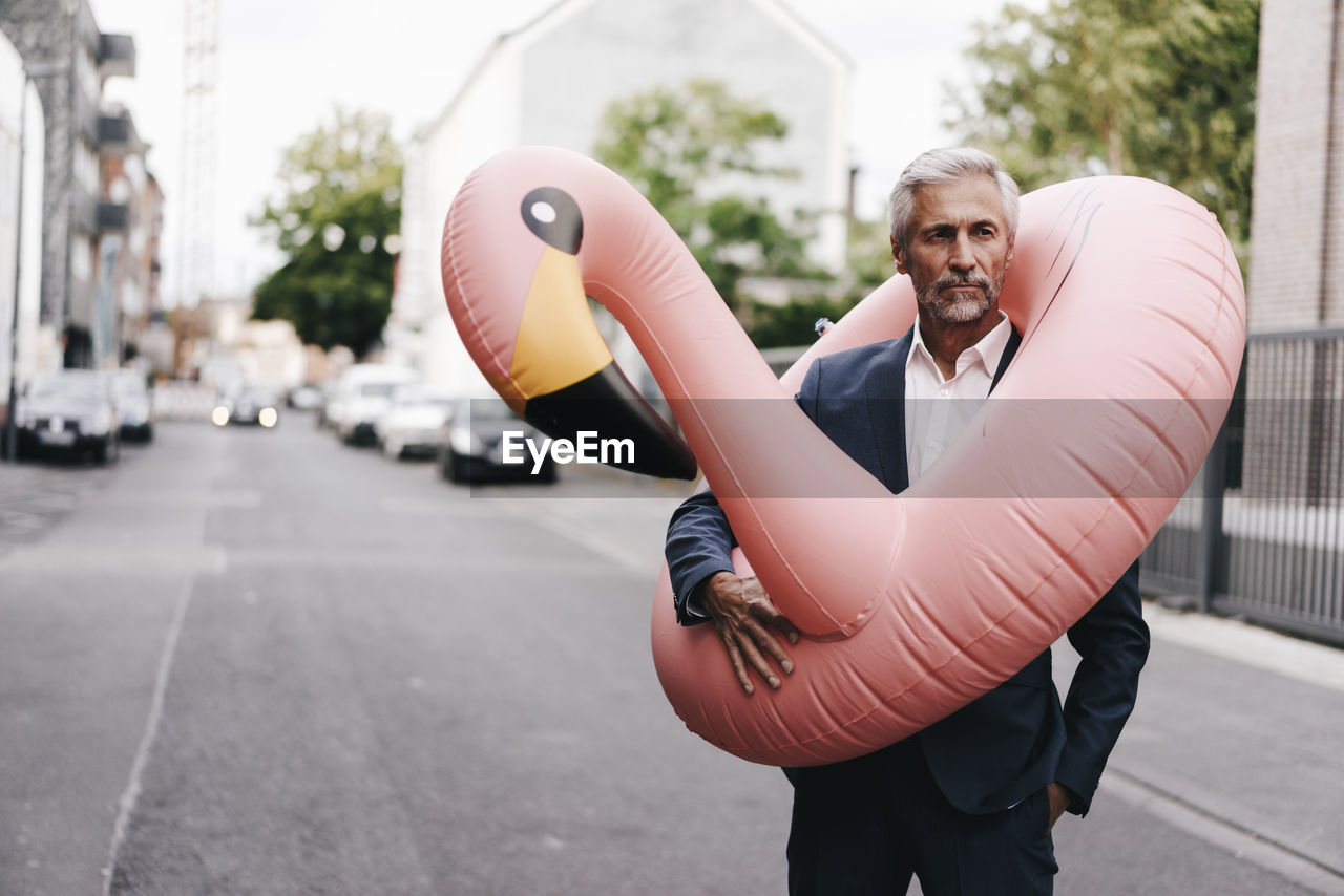 Mature businessman on the street with inflatable flamingo