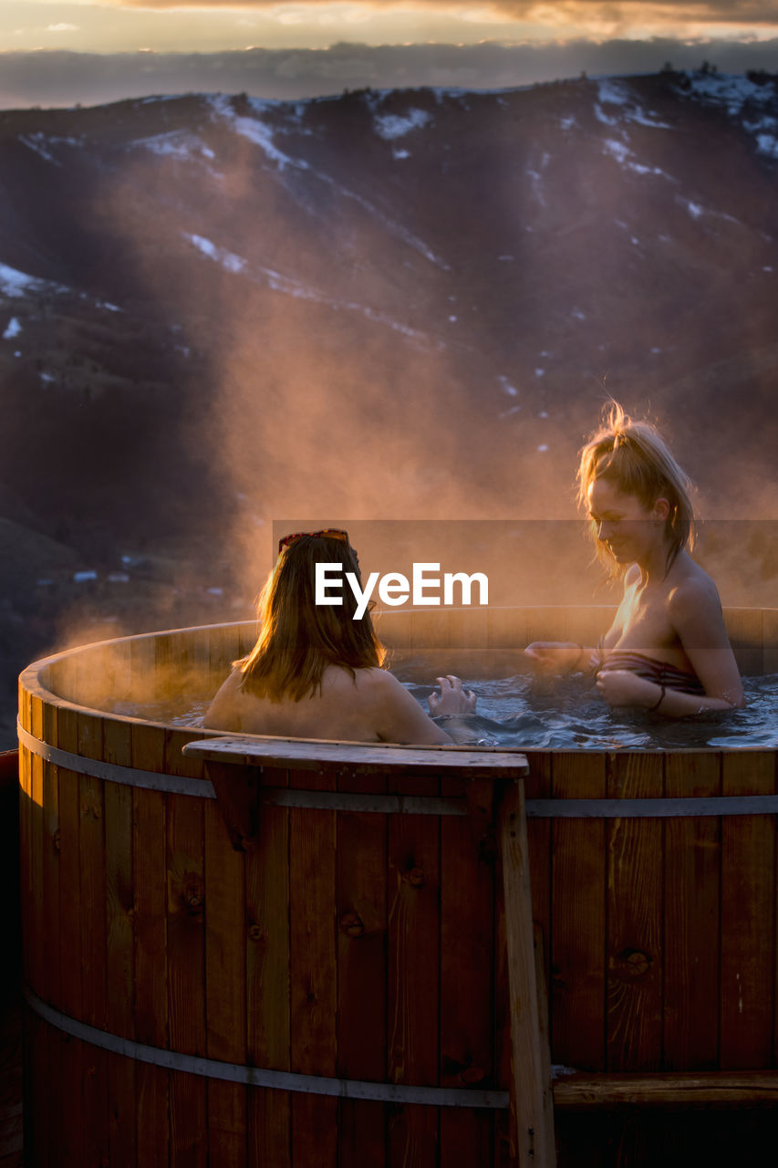 Two young women, friends, in barrels with hot water, sunset in n