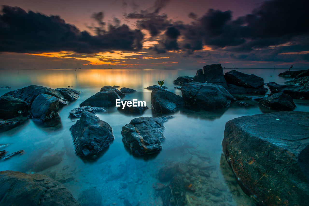 Rocks at sea shore against sky during sunset