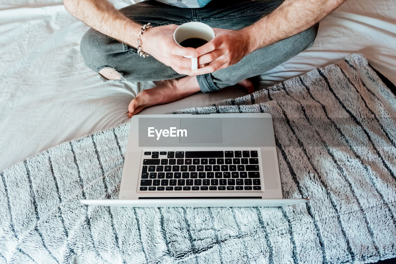 Man drinking coffee while working from bed in madrid.spain.