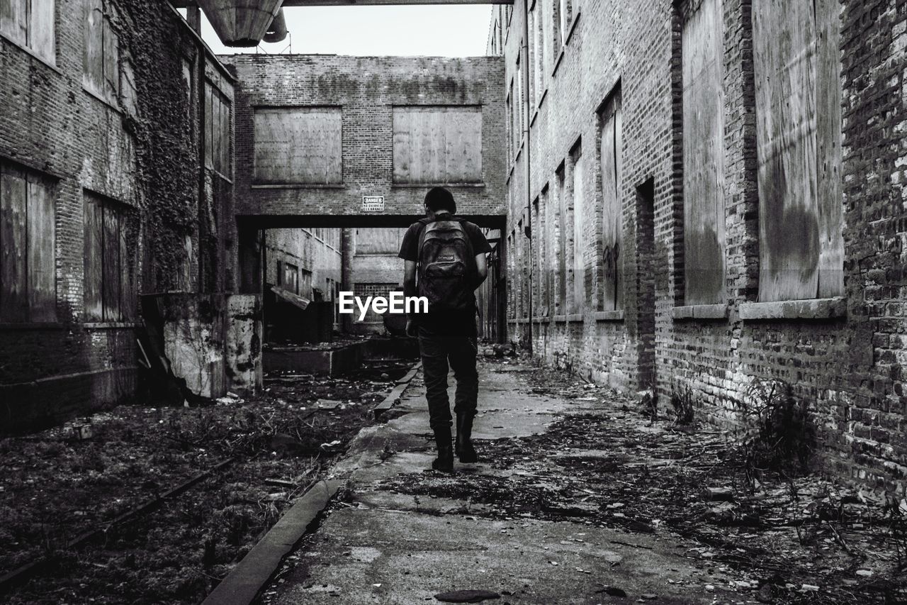 Rear view of man walking amidst abandoned buildings