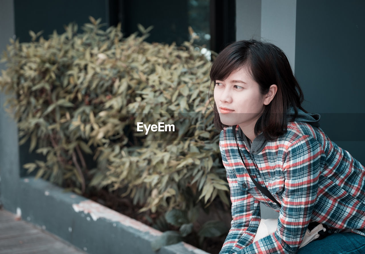 Thoughtful young woman looking away while sitting in city