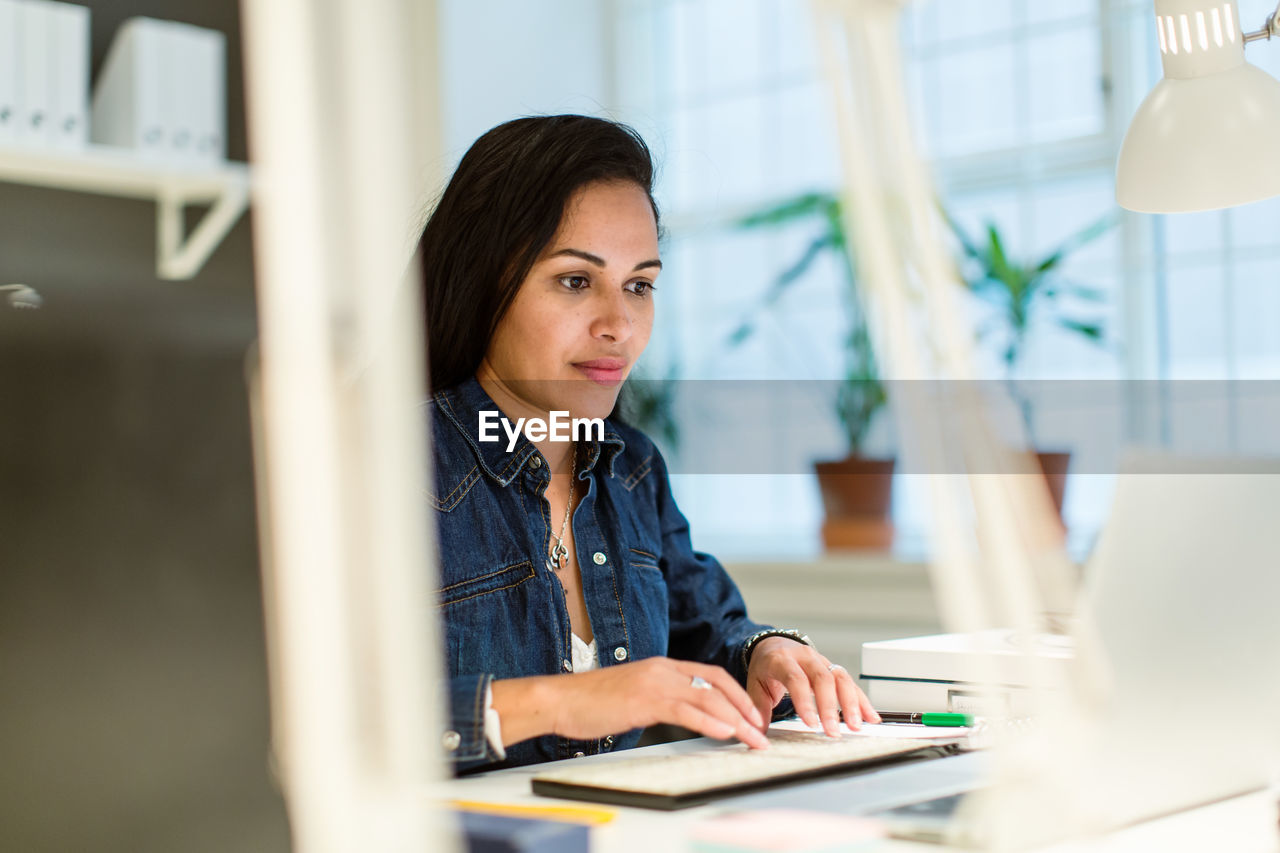 Confident businesswoman using laptop while sitting at desk in creative office