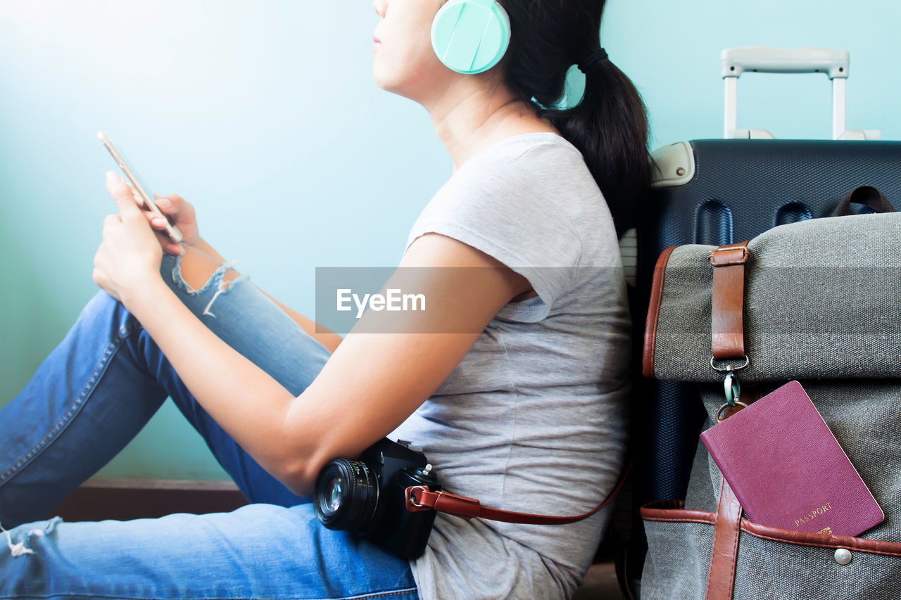 Midsection of woman using mobile phone while sitting with luggage 