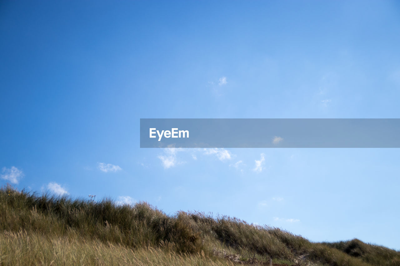 LOW ANGLE VIEW OF BLUE SKY OVER GRASSY MOUNTAIN