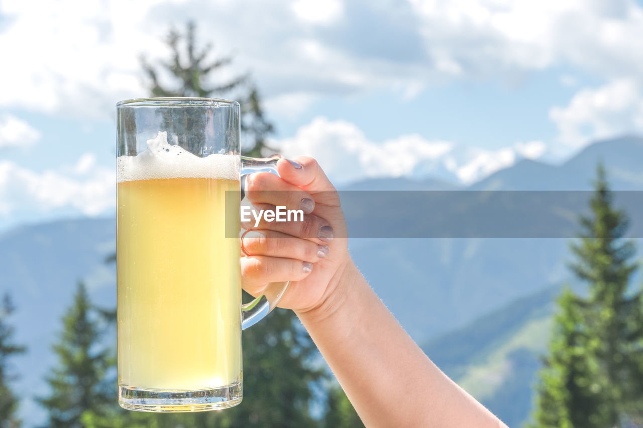 Close-up of hand holding beer glass with radler against mountain