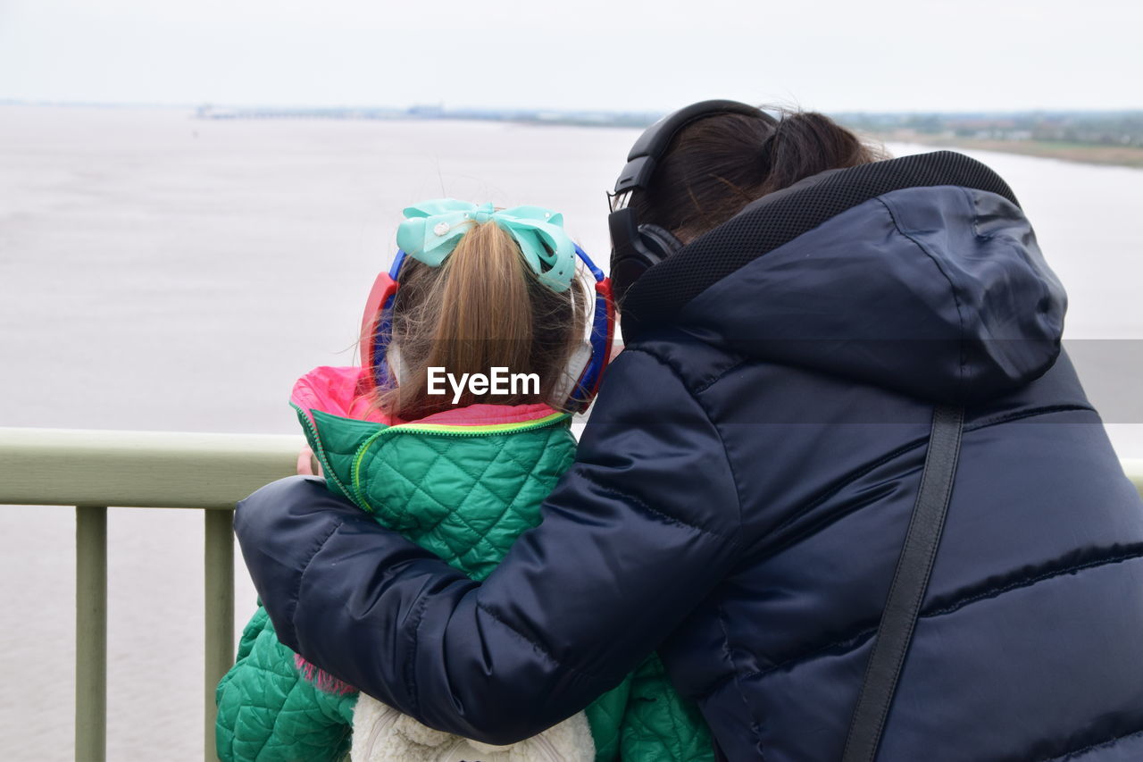 Rear view of mother and daughter against sea during winter