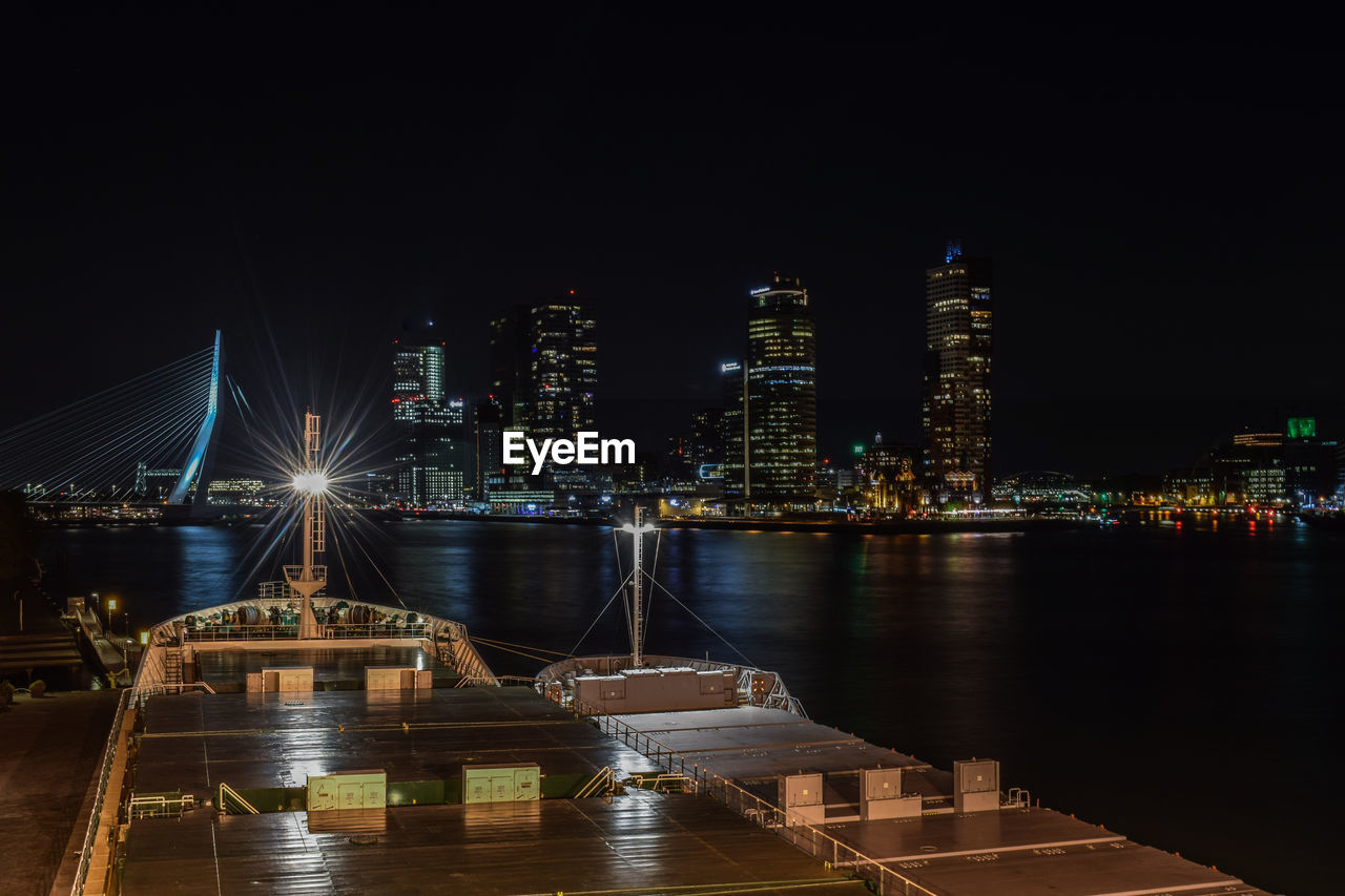 Illuminated buildings by river against sky at night