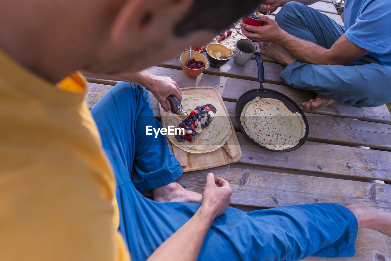 Man pouring maple syrup on sweet crepe sitting on wooden structure