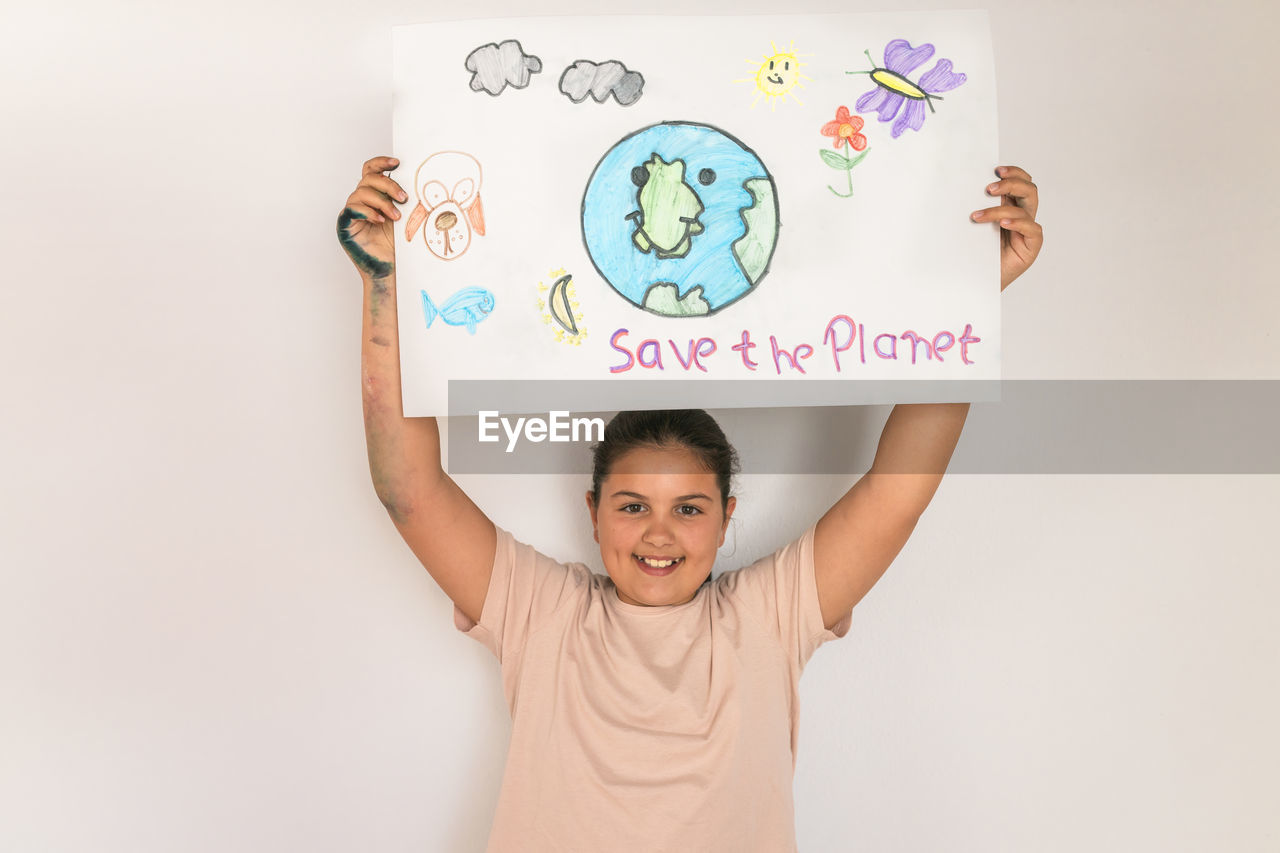 Smiling girl holding poster of environmental issues at home