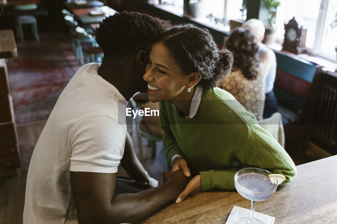 High angle view of man whispering to girlfriend at bar counter in restaurant