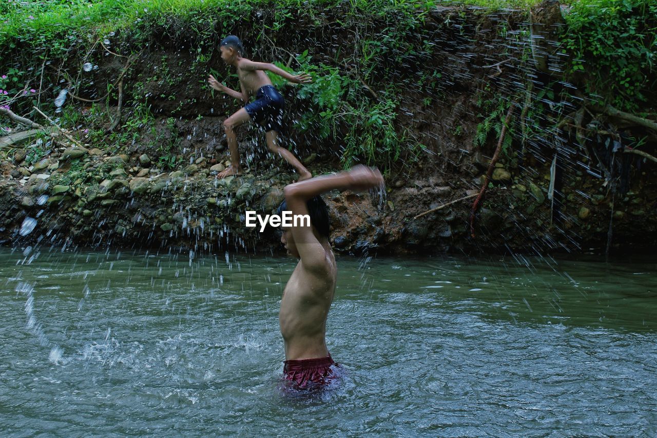 Shirtless boys playing in lake at forest