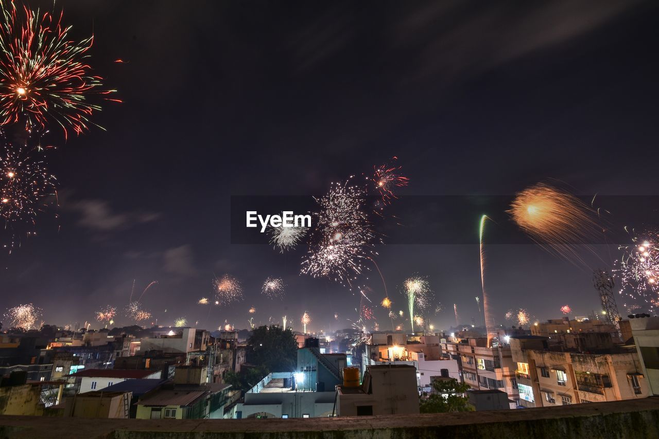 FIREWORK DISPLAY OVER ILLUMINATED BUILDINGS AGAINST SKY