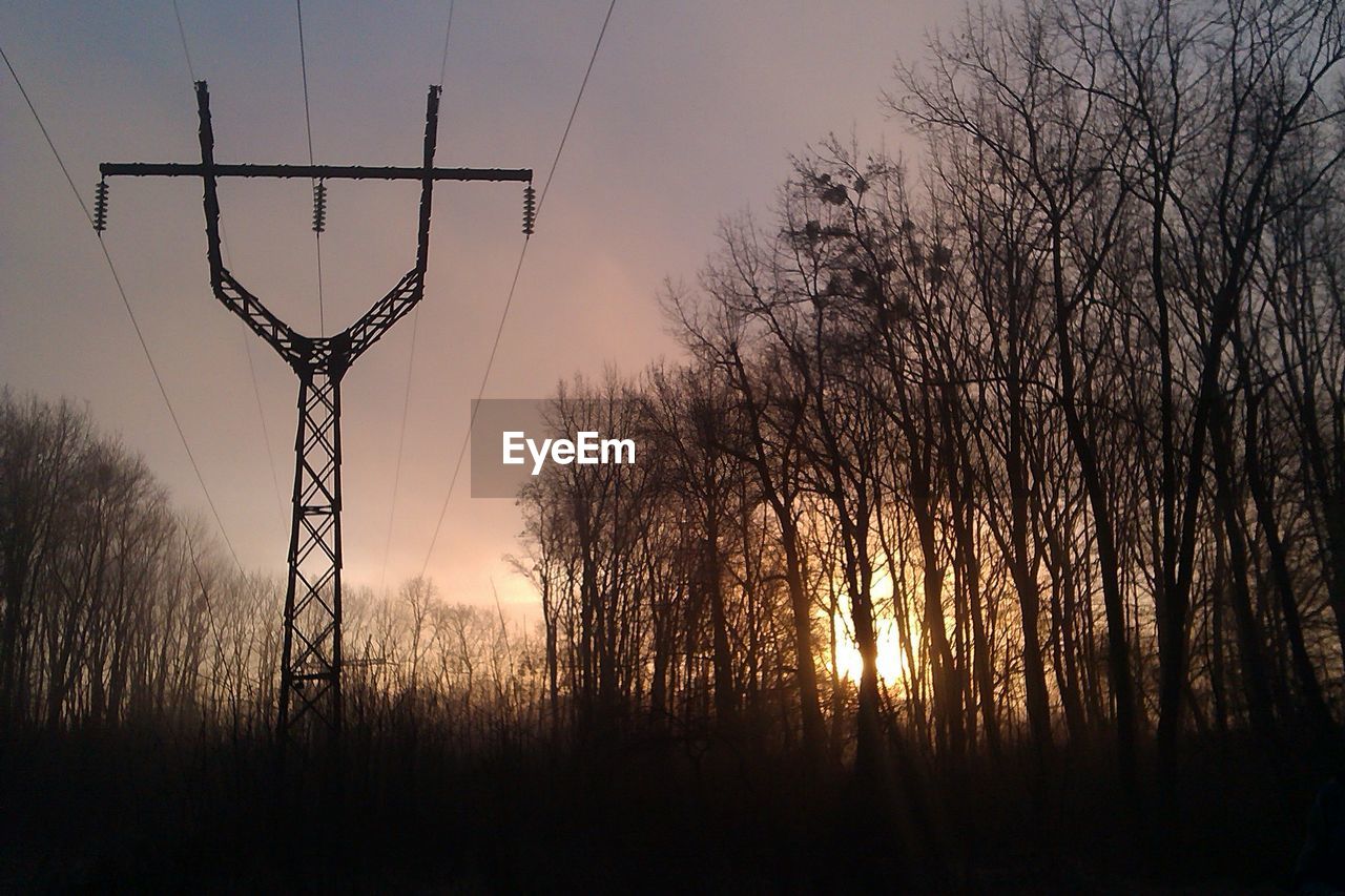 Silhouette electricity pylon by trees against orange sky