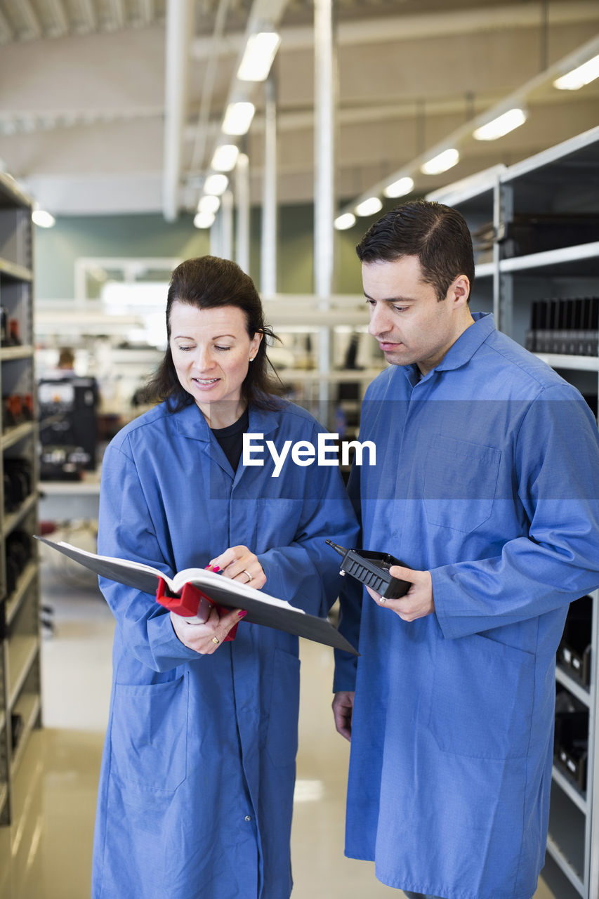 Mid adult female electrician discussing over documents with colleague in industry