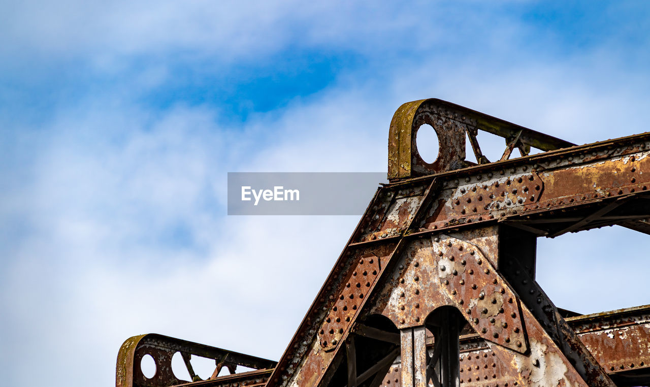 Old rusty iron bridge structure set against blue sky