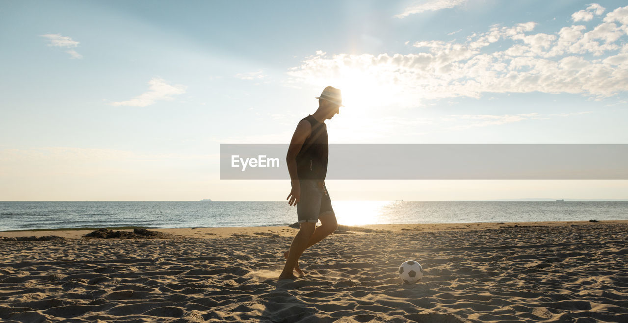 Man playing with soccer ball at beach against sky