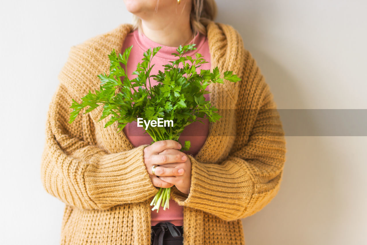 one person, adult, women, holding, clothing, studio shot, person, indoors, sweater, lifestyles, female, plant, front view, vegetable, outerwear, wellbeing, healthy eating, food and drink, standing, flower, nature, casual clothing, green, food, waist up, yellow, art, growth, freshness, hand, white background, midsection, emotion, hairstyle, portrait, leaf