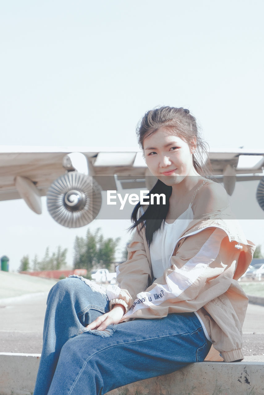 Portrait of smiling young woman sitting against clear sky