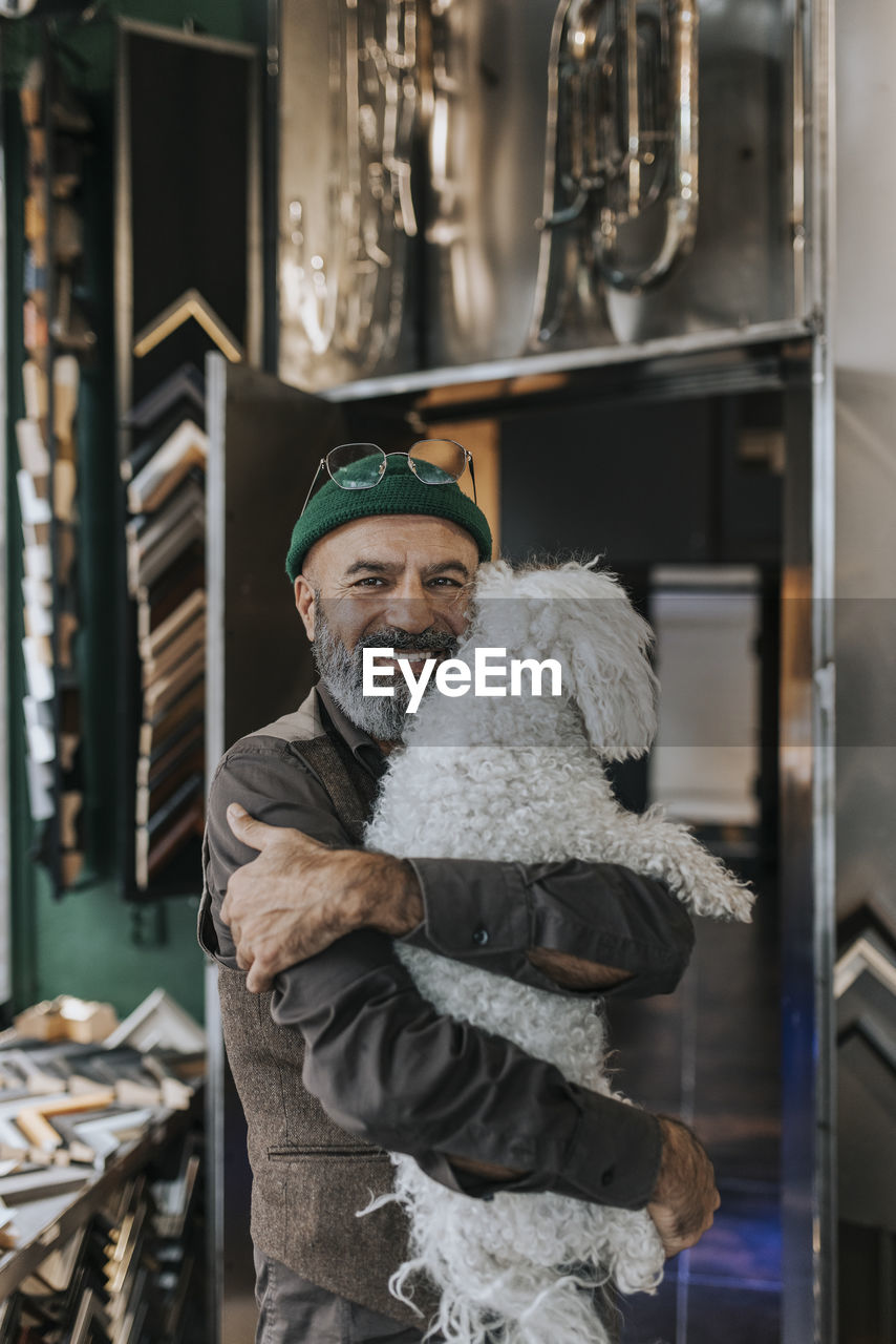 Portrait of smiling craftsman hugging pet dog in frame shop