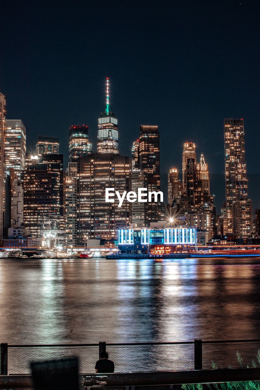 Illuminated buildings by river against sky at night