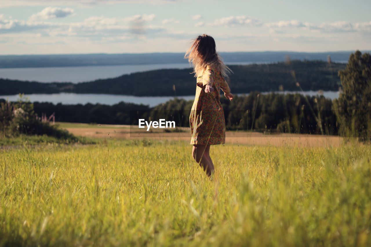 Woman with arms outstretched spinning on grassy field