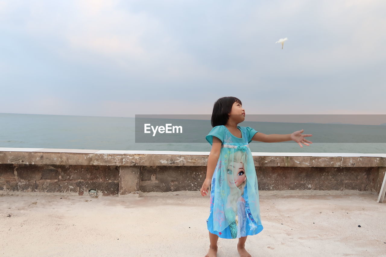 BOY STANDING AT BEACH AGAINST SKY