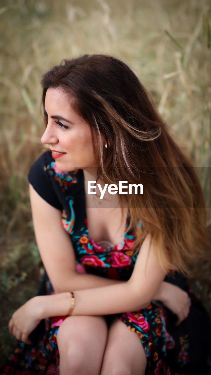 Beautiful woman looking away while sitting on field