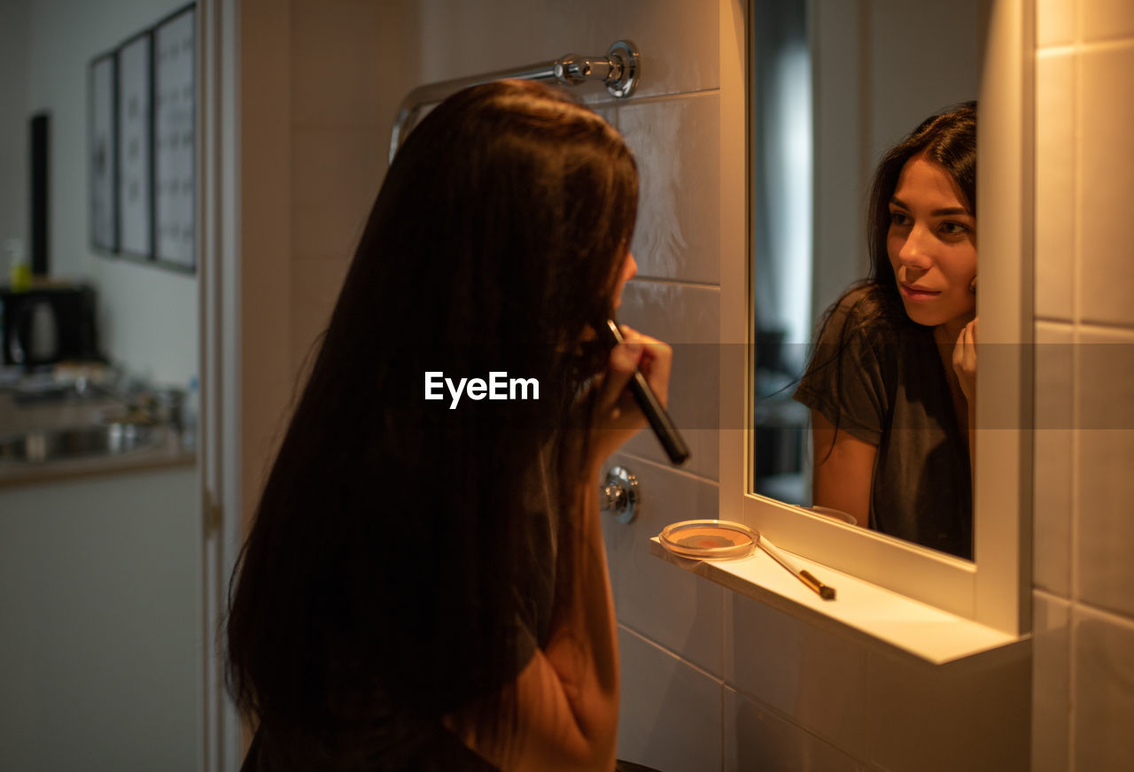 Pretty brunette female applying makeup in bathroom