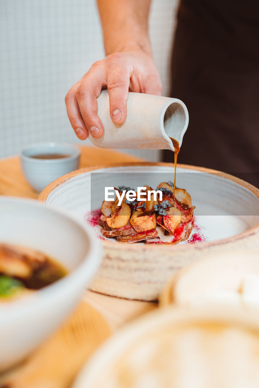 Vertical view of the unknown man hand pouring maple syrup on baked apples