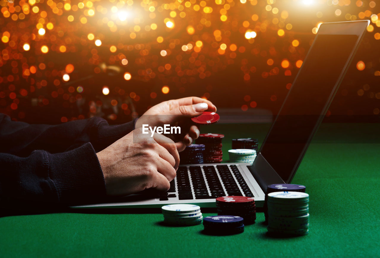 Cropped hands of woman using laptop by gambling chips