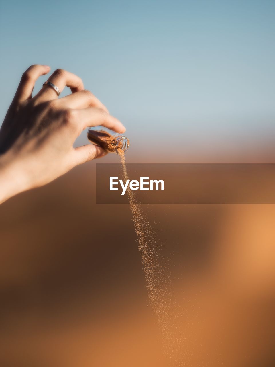 Close-up of woman hand pouring sand from bottle in desert