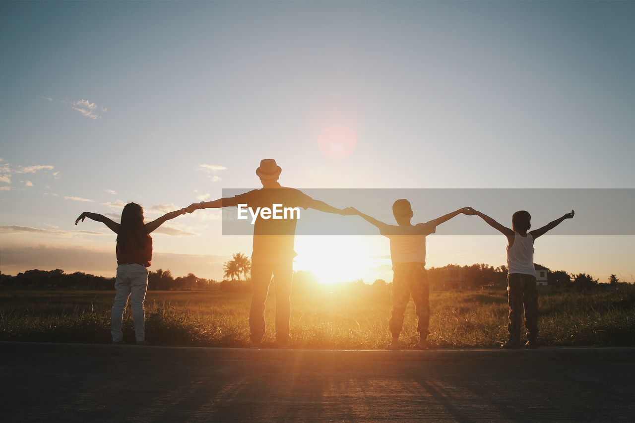 Rear view of family with holding hands while arms outstretched against sunset