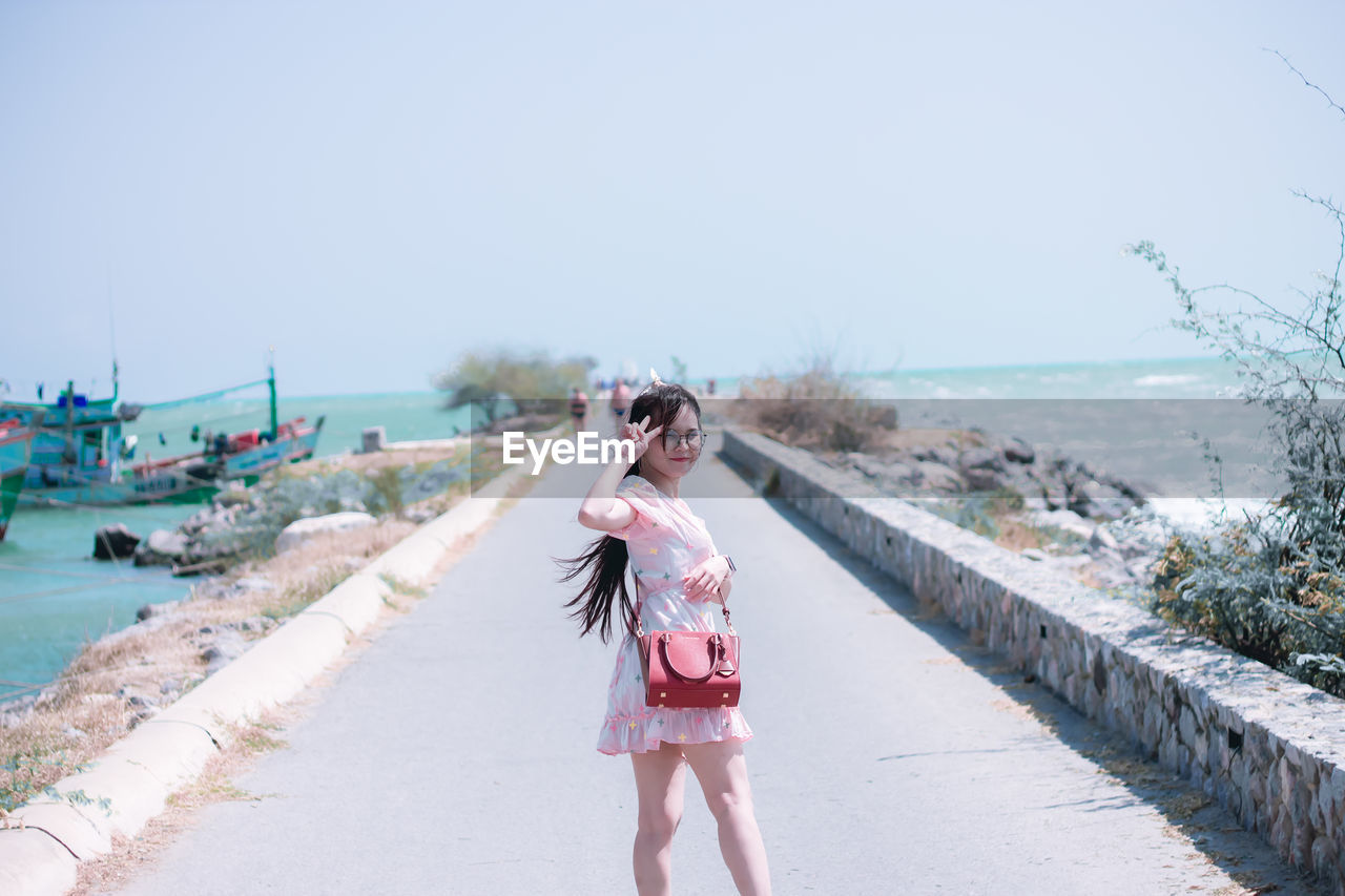Portrait of woman wearing eyeglasses standing on footpath against sea and sky