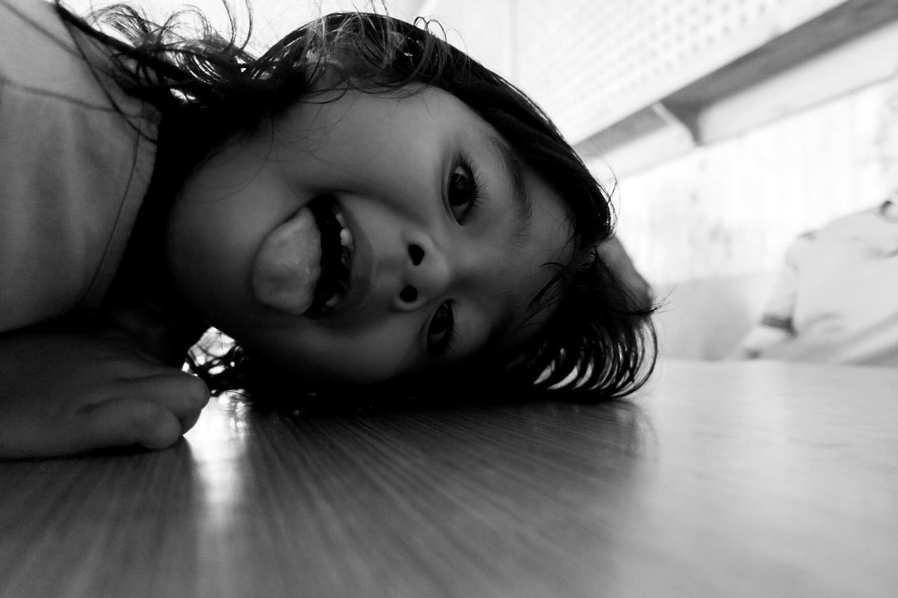Close-up portrait of girl sticking out tongue while lying on floor at home