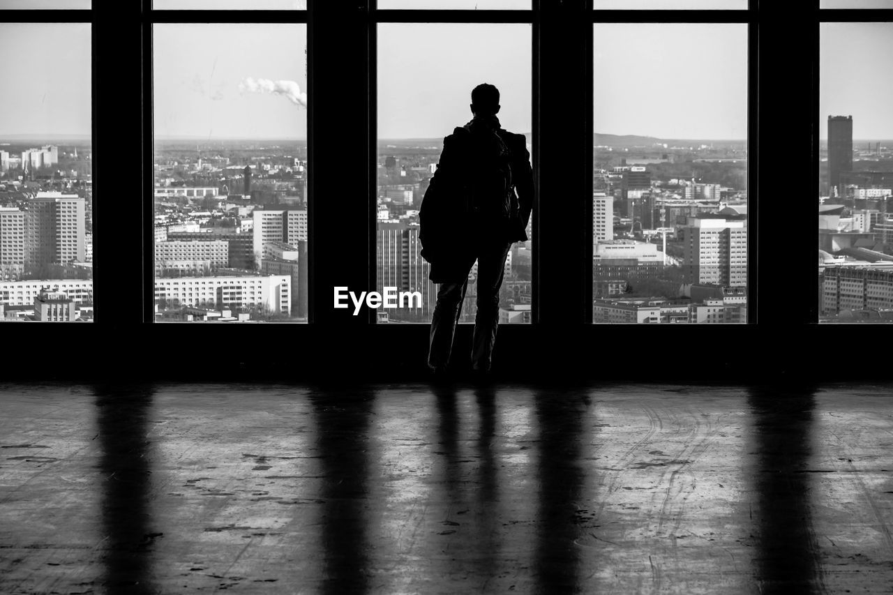 Rear view of man looking at city through window