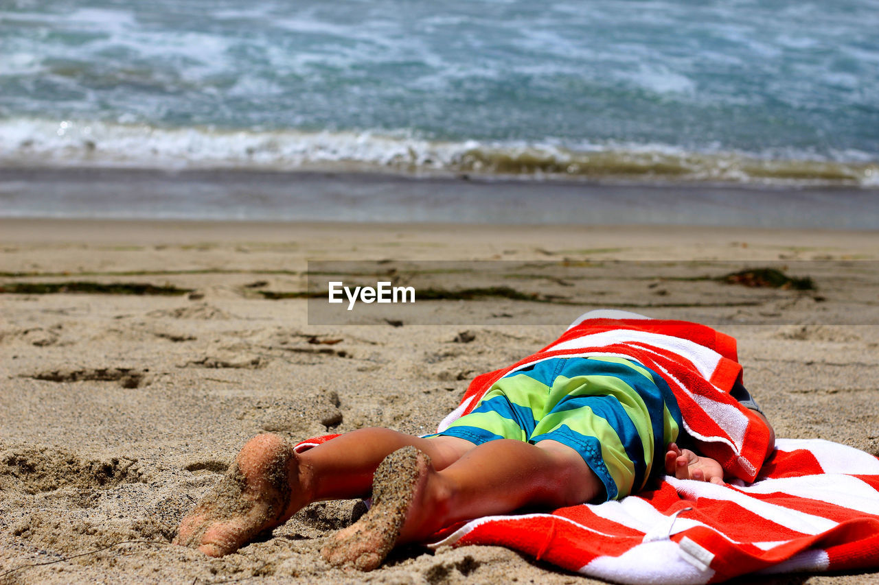 Man with towel lying on front at beach