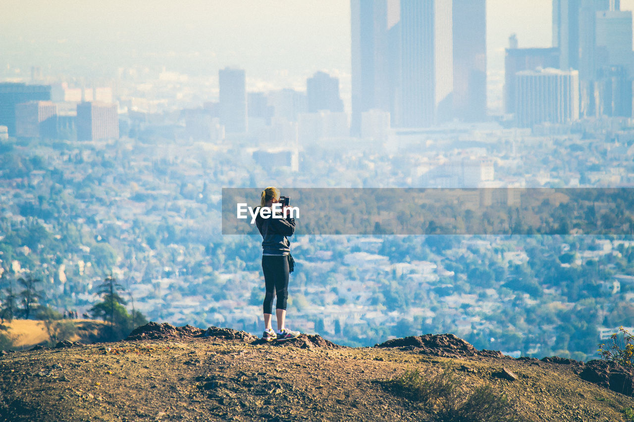 Woman photographing cityscape against sky