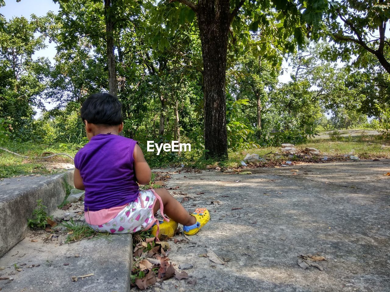 Girl sitting on street amidst trees